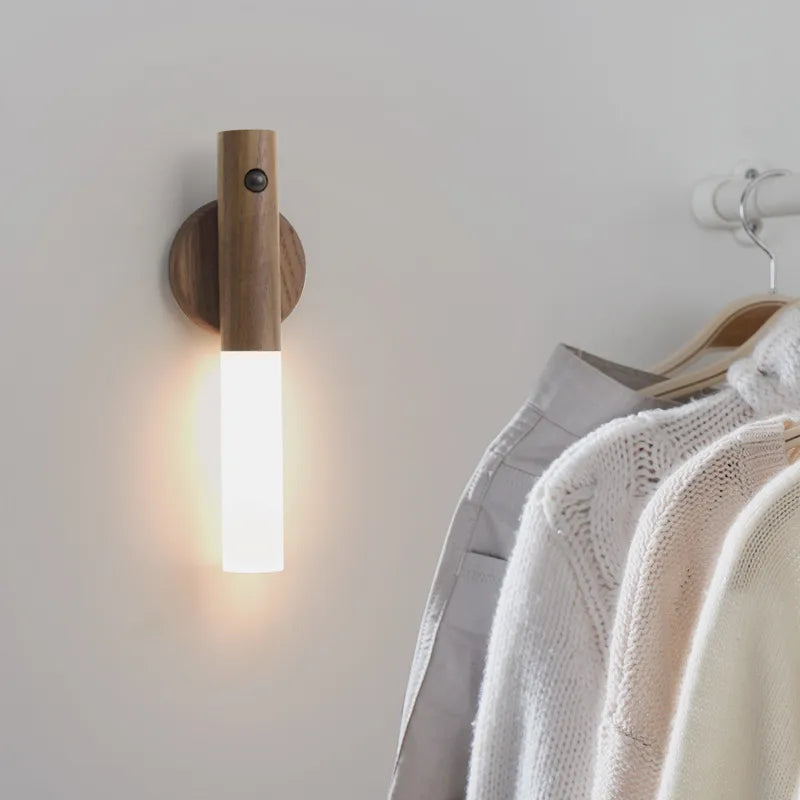 Wooden wall sconce emitting light next to a clothing rack with coats on a neutral background