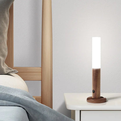 Wooden floor lamp on a nightstand next to a bed with light bedding.